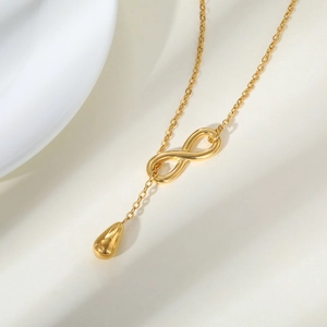Macro detail of gold infinity droplet necklace on textured beige surface