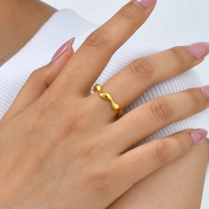 Close-up of a polished golden wavy geometric ring shown on a finger with a modern style