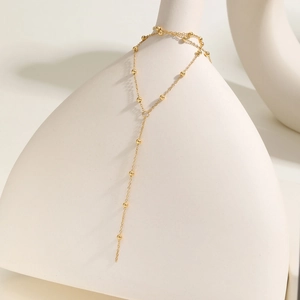 Detail of a gold Y-shaped stainless steel bead chain necklace draped on a white vase