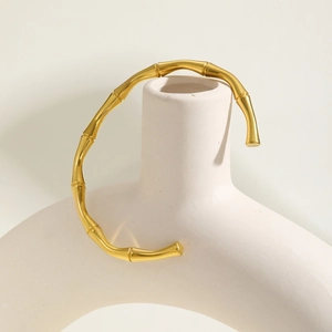 Detailed view of 18K gold C-shaped bamboo link bracelet on a white ceramic vase