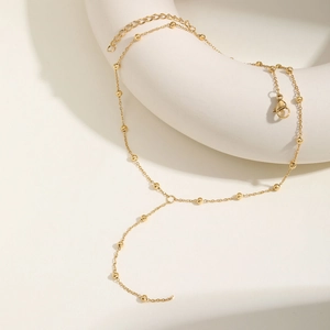 Detail of gold Y-shaped beaded necklace with lobster clasp on white ring display stand