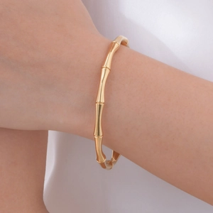 Detail shot of a polished 18K gold bamboo-style cuff bracelet on a female wrist