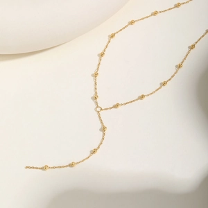 Elegant 18K gold Y-necklace with small round beads on a minimalist beige backdrop