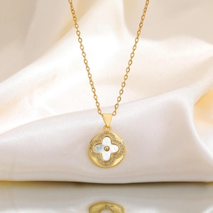 Détail d'un collier doré avec pendentif trèfle blanc rond sur fond de soie blanche