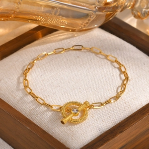 Detailed close-up of golden OT-buckle chain bracelet with single crystal on rustic linen