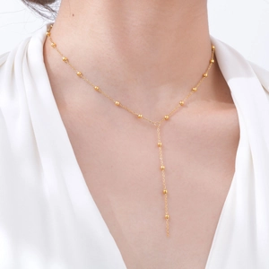 Close-up of golden Y-shaped beaded chain necklace on a model wearing a white V-neck