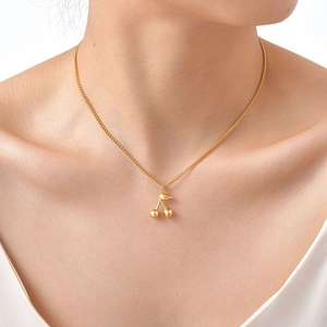Gros plan d'un collier pendentif cerise dorée porté par un mannequin montrant les détails