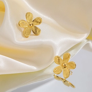 Nahaufnahme goldener Blumenohrringe mit strahlenförmigen Blütenblättern auf Satinspiegel