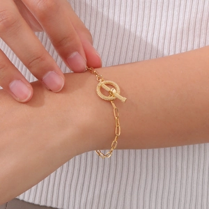 Detail of a golden OT toggle bracelet featuring a carved shell ring on a model's wrist