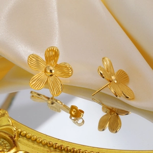 Makroaufnahme goldener Blumenohrringe mit texturierten Blütenblättern auf weißem Satin