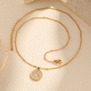 Gros plan du pendentif palmier doré sur une chaîne fine posée sur une pierre claire