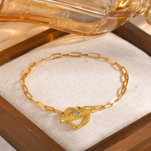 Macro shot of gold paperclip chain bracelet with a heart-shaped toggle clasp and zircon