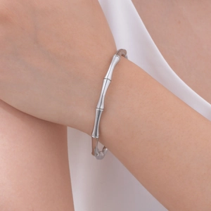 Macro shot of silver C-shaped bamboo style stainless steel bangle worn on a female wrist