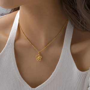 Close-up of a gold hollow flower pendant necklace on a bead chain worn by a model
