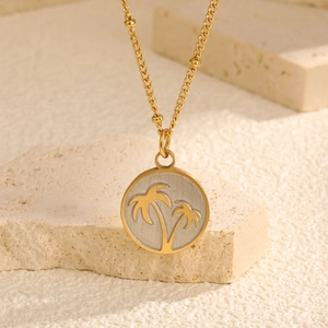 Collier en acier doré avec pendentif palmier rond sur un socle en pierre naturelle