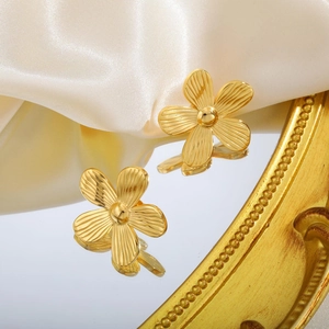 Makroaufnahme goldener Blumenohrringe mit strukturierten Blütenblättern auf Spiegel
