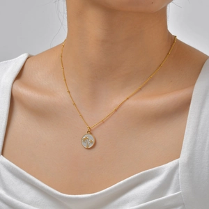 Gros plan d'un collier pendentif palmier doré avec émail blanc porté par un mannequin