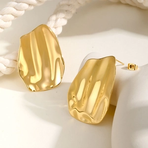 Close-up of golden irregular geometric stud earrings with a wavy hammered texture finish