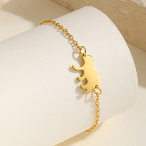 Bracelet ours minimaliste en acier inoxydable doré sur un support texturé blanc