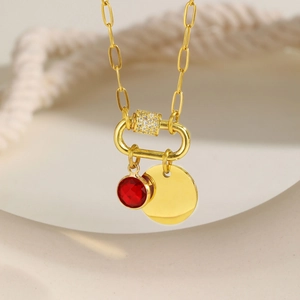 Detail of gold box chain necklace featuring a red round stone and blank round pendant