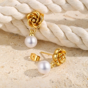 Detail of gold camellia flower earrings with white pearl drop on rustic stone background