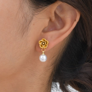Elegant gold camellia flower earrings with a white round pearl pendant on model