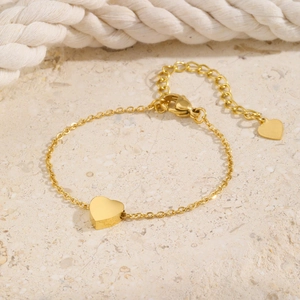 Detailed view of a gold heart pendant anklet with adjustable chain on a textured surface