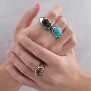 Close-up of three men's stainless steel rings featuring black onyx, turquoise, and tiger eye