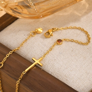 Detailaufnahme des goldenen Kreuzarmbands mit rotem Geburtsstein und Karabinerverschluss