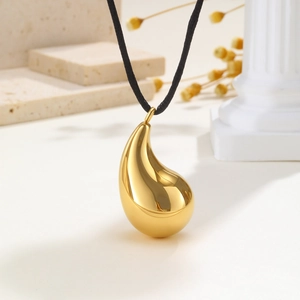 Macro detail of gold teardrop pendant with black braided rope on a stone background