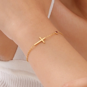 Makroaufnahme Goldarmband mit Kreuz und rotem Edelstein am Handgelenk einer Frau