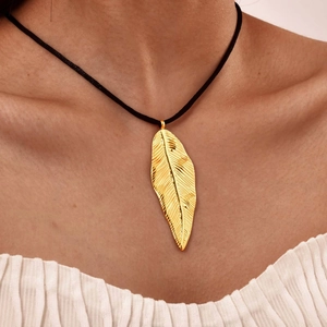 Dettaglio del ciondolo a piuma in oro 18K sulla pelle con trama incisa delicata