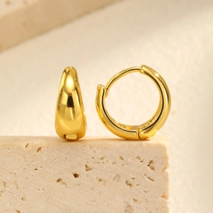 Macro view of minimalist golden U-shaped huggie earrings on a stone textured stand