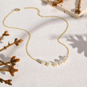 Close-up of double-layer copper necklace with five pearls on a white textured background