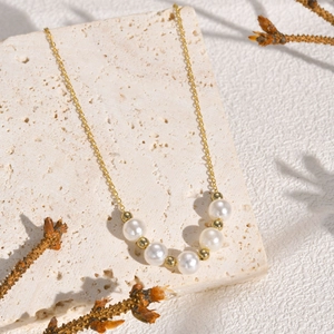 Close-up of double layer gold necklace with white pearls on a minimalist stone background