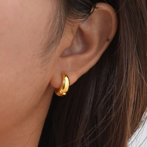 Close-up of a minimalist chunky gold U-shaped hoop earring on a model's ear