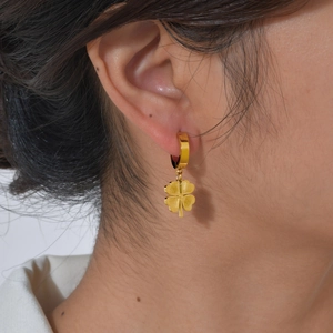 Vue macro de boucles d'oreilles trèfle à quatre feuilles dorées portées par un mannequin