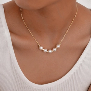 Detailed close-up of a double-layered pearl necklace with golden spherical beads on a model