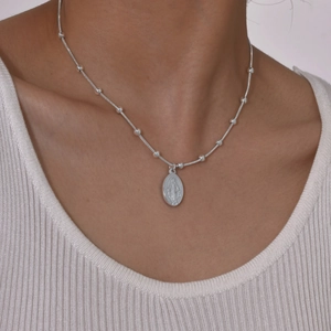 Detail van zilveren slangenschakelketting met Maria-hanger gedragen door model op wit topje