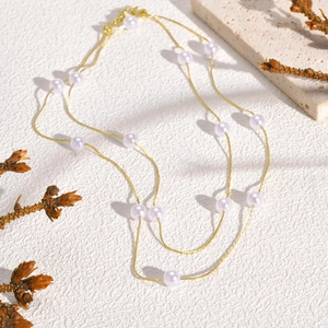 Elegant double-layered gold chain necklace with white pearls on a textured background