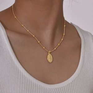 Detail van een gouden slangenketting met kralen en een Maria-medaille op een model