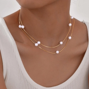 Close-up of elegant double-layered gold necklace with white pearls on a model's neck