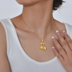 Close-up of golden cherry pendant necklace worn by model on a minimalist background