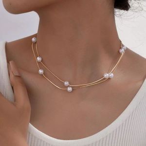 Detail of elegant gold-tone layered necklace featuring white pearls on a female model