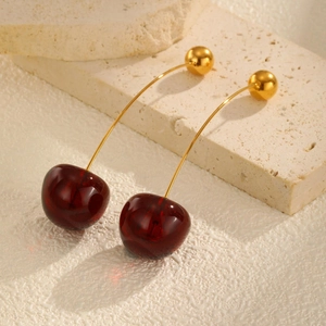 Detailed view of red cherry-shaped drop earrings with golden stems on stone background