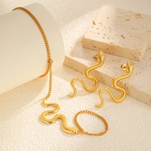 Minimalist gold snake jewelry set with necklace earrings and ring on stone pedestal