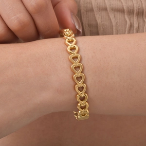 Detailed view of an 18K gold hollow heart bracelet on a wrist with intricate floral patterns
