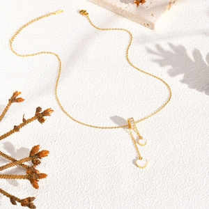 Détail d'un collier en titane doré avec pendentifs doubles coeurs sur surface en pierre