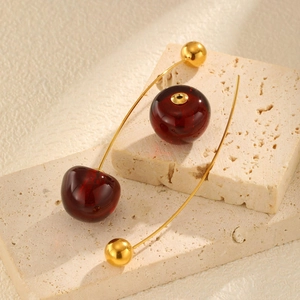 Detail of red cherry earrings with gold curved rods on a beige textured stone background
