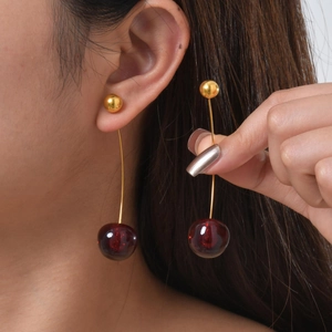 Detail of elegant gold cherry drop earrings with deep red translucent beads on a model